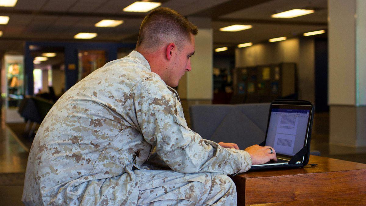 穿着军装的男学生在图书馆用笔记本电脑工作
