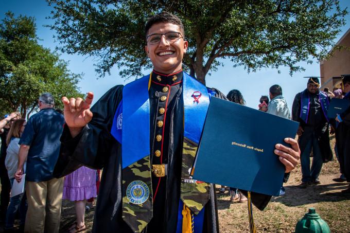 一名ROTC学生在2022年春季毕业典礼上举起公羊手微笑.